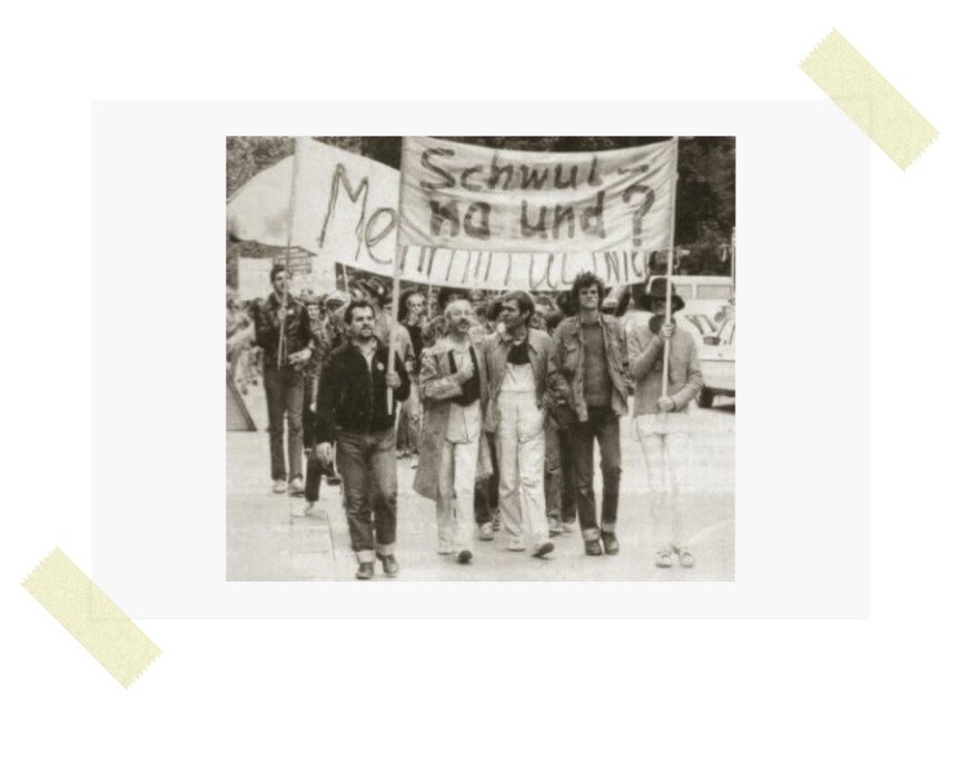 QueerPflege-LSBTIQ-Pflege Eine Gruppe von Menschen marschiert mit einem Banner, auf dem ein Text für LSBTIQ-Pflege steht. Das Bild ist schwarzweiß.