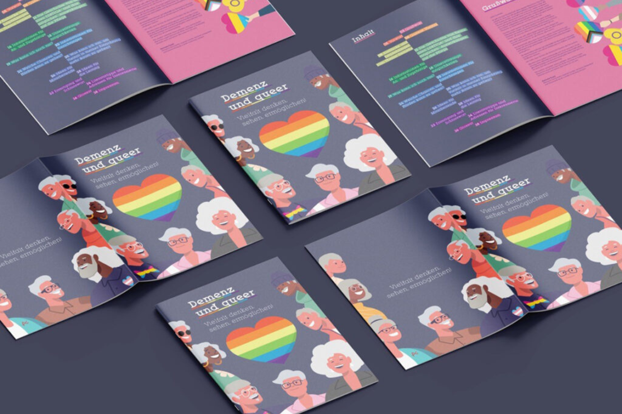 QueerPflege-LSBTIQ-Pflege Ein Display mit Broschüren mit dem Titel „Demenz und Queer“ mit Abbildungen unterschiedlicher Menschen rund um ein Herz in Regenbogenfarben. Die Broschüren liegen in verschiedenen Positionen auf einer flachen Oberfläche.